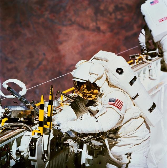 Astronaut James Newman works with power ratchet tool in payload bay