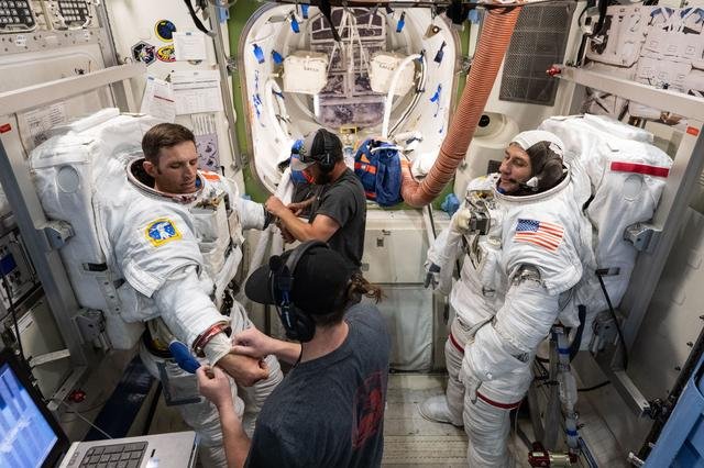 Trainers assist astronauts Josh Kutryk and astronaut Luke Delaney  as they practice suiting up in spacesuits